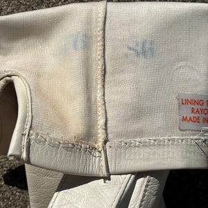 May include: Close-up of a white fencing glove, showing the interior lining and exterior leather. The glove has a stitched seam and a label with text. There are blue stains on the fabric.