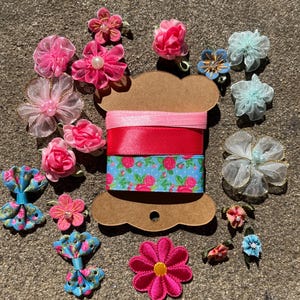 Può includere: Un assortimento di abbellimenti floreali colorati e nastri. L'immagine presenta vari fiori di tessuto rosa, blu e bianchi, insieme a una bobina di nastri rosa, rossi e a fantasia floreale. Questi articoli sono ideali per l'artigianato e l'abbellimento.