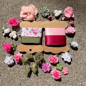 Pode incluir: Uma variedade de materiais de artesanato, incluindo rolos de fita e flores de tecido. As fitas são em tons de rosa, vermelho e verde, algumas com estampas florais. As flores são de vários tamanhos e cores.