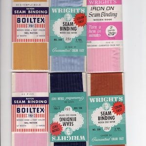 May include: A collection of vintage seam binding rolls in various colors, including gold, blue, pink, and brown. Each roll is labeled with the brand name and product details. The packaging features text such as "Woven Edge" and "Color Fast".
