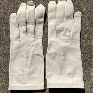 May include: A pair of white leather gloves. Each glove has a decorative embroidered leaf design near the wrist. The gloves are made of a smooth, soft leather and appear to be in good condition.