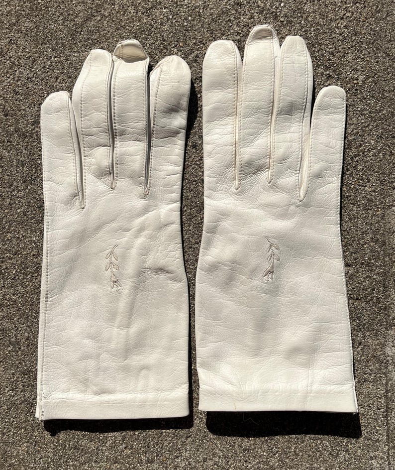 May include: A pair of white leather gloves. Each glove has a decorative embroidered leaf design near the wrist. The gloves are made of a smooth, soft leather and appear to be in good condition.