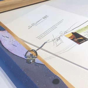 May include: A close-up of a framed canvas painting with a hanging wire and a metal D-ring. The back of the frame is visible, showing a white card with the text "SBrownART..." and a signature. The text "Thank you for supporting Fine Art by Stacy Brown. Your purchase helps support my art career. Look forward to sharing more of my work with you via www.staceybrownart.com for new images." is also visible on the card.