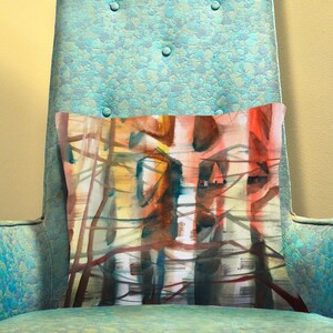 K&ouml;nnte beinhalten: Ein rechteckiges Kissen mit einem abstrakten Aquarelldesign in Rot-, Orange-, Braun- und Gelbt&ouml;nen. Das Kissen liegt auf einem tealfarbenen Sessel mit Knopfdetails. Das Kunstwerk erinnert an eine Waldszene.