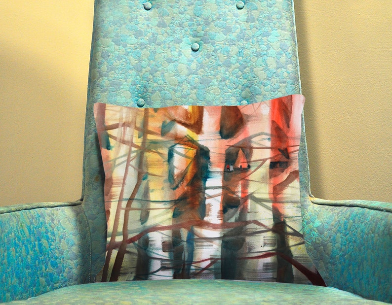 K&ouml;nnte beinhalten: Ein rechteckiges Kissen mit einem abstrakten Aquarelldesign in Rot-, Orange-, Braun- und Gelbt&ouml;nen. Das Kissen liegt auf einem tealfarbenen Sessel mit Knopfdetails. Das Kunstwerk erinnert an eine Waldszene.