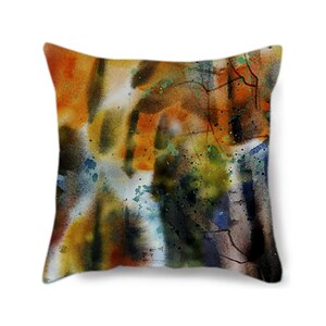 May include: Square throw pillow with an abstract watercolor design. The pillow features a blend of warm colors, including orange, yellow, and brown, with accents of blue and green. The design has a textured appearance, resembling brushstrokes and splatters.