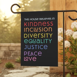 May include: A black garden flag with the text "This house believes in" and the words "kindness", "inclusion", "diversity", "equality", "justice", "peace", and "love" in rainbow colours.