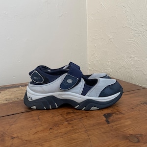 May include: A pair of blue and grey athletic shoes with a hook-and-loop strap. The shoes have a chunky sole and the brand logo is visible on the side.