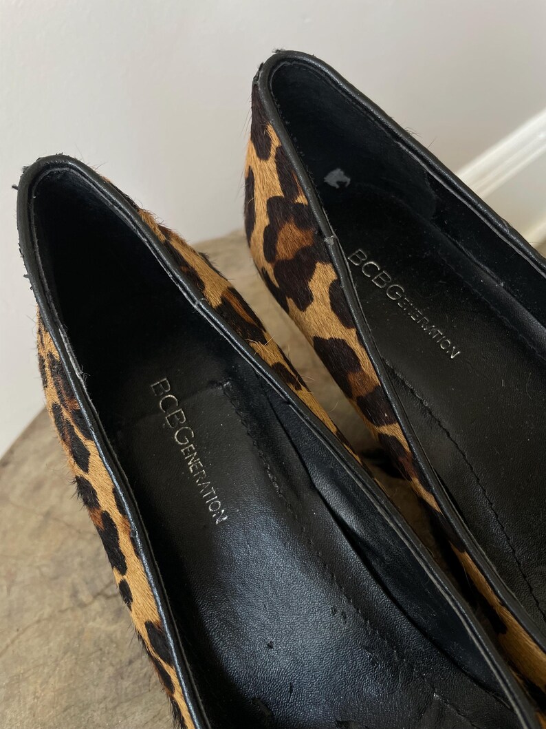 May include: A pair of BCBGeneration pumps featuring a textured leopard print pattern in shades of tan, brown, and black. The interior of the shoes is lined with black material, and the brand name BCBGeneration is printed in white on the black insoles.