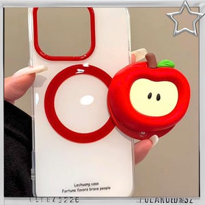 Puede incluir: Funda de teléfono transparente con detalles rojos y un soporte para teléfono en forma de manzana roja. La funda tiene el texto "Lechuang case Fortune favors brave people". El agarre de la manzana tiene un centro amarillo claro con dos puntos negros.
