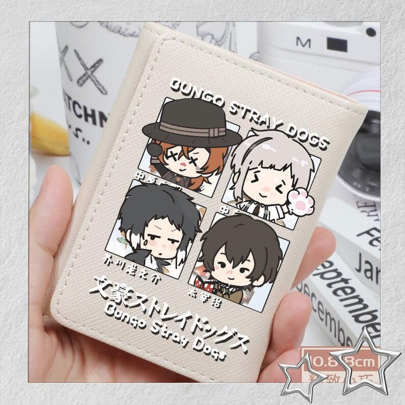 Puede incluir: Cartera beige con ilustraciones de personajes de dibujos animados y texto japon&eacute;s, incluyendo "Bungo Stray Dogs". La cartera tiene aproximadamente 0,8 cm de grosor. Tambi&eacute;n se ve el texto "GUNGO STRAY DOGS".