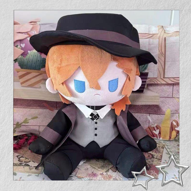 以下が含まれることがあります： オレンジ色の髪、青い目、黒い帽子をかぶったキャラクターのぬいぐるみ。人形はグレーのベスト、黒いジャケット、ズボンを着ています。人形は花柄の表面に座っています。