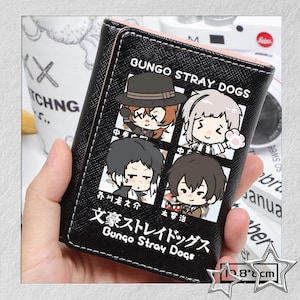 Puede incluir: Cartera negra con interior rosa, con personajes de dibujos animados de "Bungo Stray Dogs." El dise&ntilde;o incluye cuatro retratos de personajes y el texto "Bungo Stray Dogs." Mide aproximadamente 10,8 cm x 8 cm.