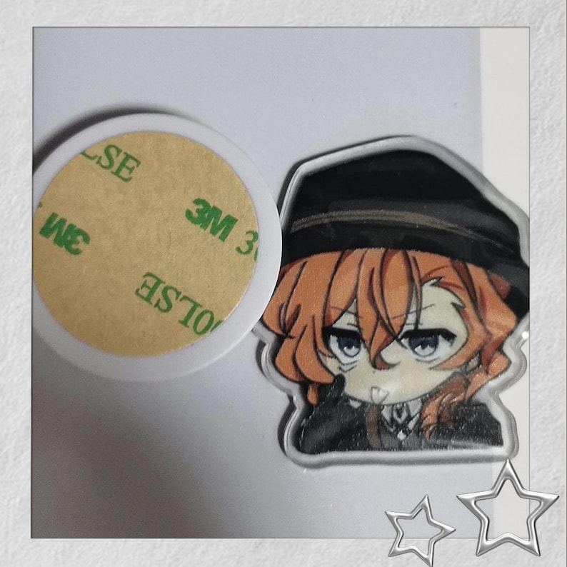May include: A clear acrylic charm featuring an anime character with orange hair and a black hat. The charm is next to a white adhesive circle with the text "3M" and "SE".
