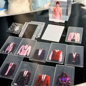 May include: A collection of clear acrylic display items, including photo holders and cards featuring images of various suit jackets and a shirtless person. The items are arranged on a dark surface.