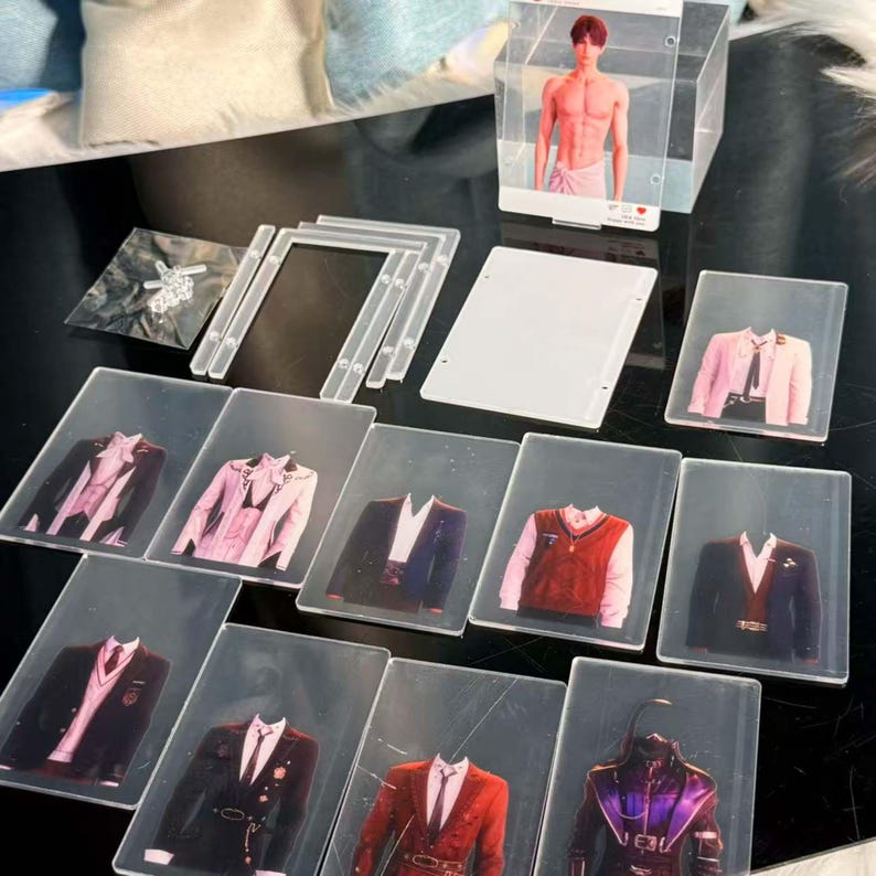 May include: A collection of clear acrylic display items, including photo holders and cards featuring images of various suit jackets and a shirtless person. The items are arranged on a dark surface.