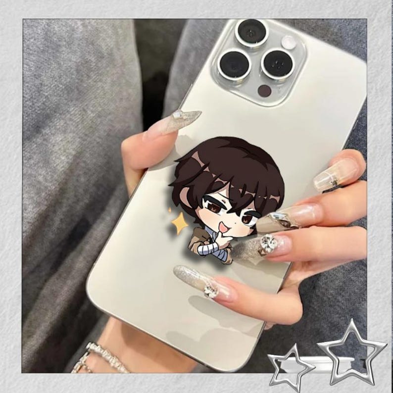May include: A white smartphone with a cartoon character pop-socket attached. The pop-socket features a brown-haired anime character with a light brown jacket and a blue bandage. The phone has three camera lenses.