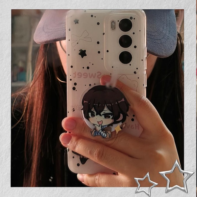 May include: Clear phone case with a cartoon character pop socket. The case has a white background with black dots and stars. The pop socket features a brown-haired anime character with a blue and white outfit.