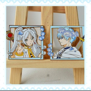 May include: Two anime-style character pins. One pin features a female character with long white hair and a gold and white outfit. The other pin depicts a male character with blue hair and a flower crown, wearing a white and blue outfit.
