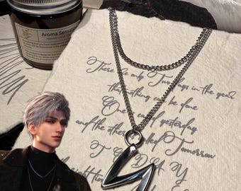 May include: A silver-toned layered necklace with a geometric pendant. The pendant is shaped like the letter "Z". The necklace is displayed on a textured paper with handwritten script. A jar of scented candle is in the background.