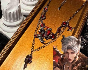 May include: A gothic-style necklace with a dark metal chain and red gemstone accents. The necklace features a central pendant with a dragon design and a long, ornate drop. The jewelry is displayed on a gold-toned tray.