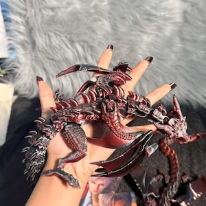 Op de afbeelding: Gedetailleerd, beweeglijk drakenbeeldje in rood en zwart. De draak heeft ingewikkelde schubben, vleugels en een slangachtig lichaam. Het beeldje wordt in een hand gehouden, wat de grootte en details laat zien.