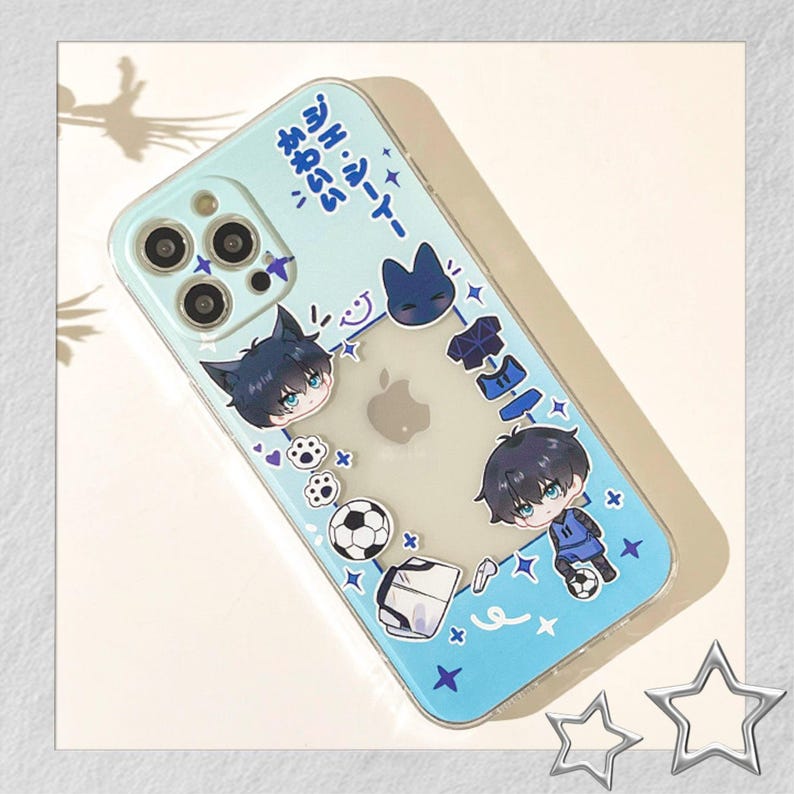 Peut inclure: Coque de t&eacute;l&eacute;phone transparente avec un bord bleu clair et un motif de personnages de style anime, de ballons de football et de texte japonais. L'&eacute;tui a un centre transparent, mettant en valeur le logo Apple du t&eacute;l&eacute;phone.