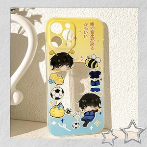 Peut inclure: Coque de t&eacute;l&eacute;phone jaune et bleue avec des graphiques de dessins anim&eacute;s d'abeilles et de ballons de football. La coque pr&eacute;sente du texte japonais et des illustrations d'un personnage en uniforme de football bleu.