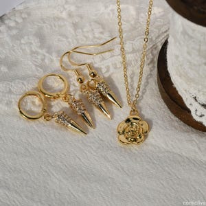 May include: A gold necklace with a rose pendant and a pair of gold earrings with a pointed, crystal-encrusted design.