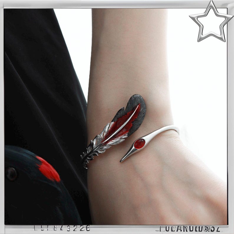 Puede incluir: Una pulsera de plata con dise&ntilde;o de pluma roja y negra y un acento de piedra preciosa roja. La pulsera se envuelve alrededor de la mu&ntilde;eca, mostrando una pieza de joyer&iacute;a elegante y art&iacute;stica.