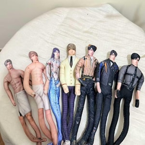 Peut inclure: Une collection de poupées en tissu faites à la main, chacune avec des tenues et des coiffures uniques. Les poupées comprennent une sirène, une poupée en cardigan et cravate, et des poupées dans diverses tenues modernes. Les poupées sont disposées en rangée.