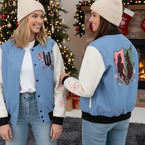 May include: Two light blue and white letterman jackets with black trim are shown. One jacket has a large "W" with butterflies and text on the sleeve. The other jacket has a crest design on the back. Both jackets are worn by people wearing beige beanies.