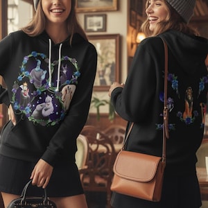 May include: Black hooded sweatshirt featuring a colorful wreath design with cartoon characters. The front of the sweatshirt displays a circular design with several characters. The back of the sweatshirt has a similar design. The sweatshirt has a drawstring hood and a front pocket.