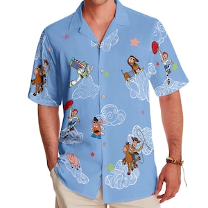 May include: A light blue short-sleeved button-down shirt with a white cloud and star pattern. The shirt features characters from the Toy Story franchise, including Woody, Buzz Lightyear, and Jessie.