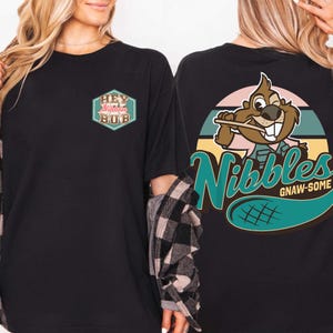 May include: Black t-shirt with a graphic on the front that says "Hey Nibbles Bub" in a hexagon shape. The back of the shirt has a cartoon beaver with the word "Nibbles" and "Gnaw-Some" in a teal color.
