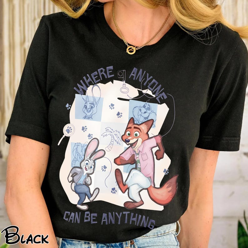 Pode incluir: Camiseta preta com personagens de desenho animado de Zootopia. O design inclui Judy Hopps e Nick Wilde, com o texto "WHERE ANYONE CAN BE ANYTHING". A camiseta &eacute; de gola redonda.