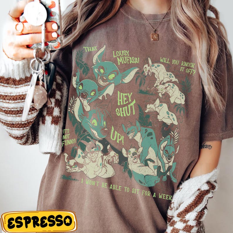 May include: Espresso-colored t-shirt featuring a graphic of cartoon hyenas with text that reads "That Lousy Mufasa!" and "Hey Shut Up!" Other text includes "It's Not Funny!" and "I Won't Be Able To Sit For A Week."