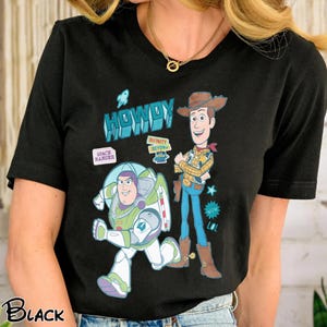 Peut inclure: T-shirt noir avec un motif de Woody et Buzz l'&Eacute;clair de Toy Story. Le motif comprend le mot "HOWDY" et les phrases "SPACE RANGER" et "INFINITY & BEYOND". Le t-shirt est &agrave; col rond.