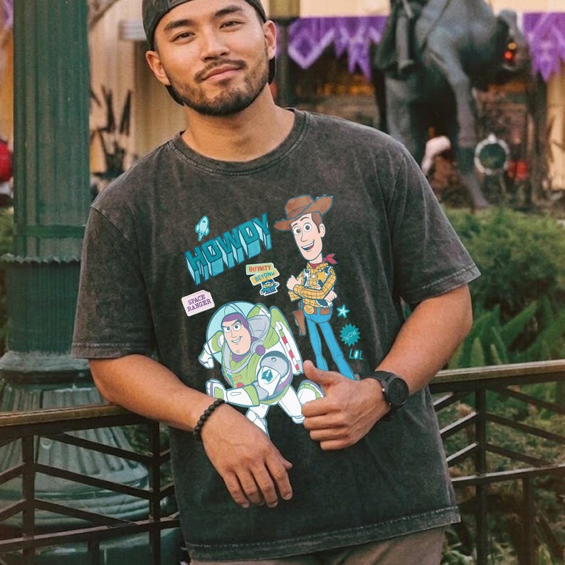 Peut inclure: T-shirt gris fonc&eacute; avec les personnages de dessins anim&eacute;s Buzz l'&Eacute;clair et Woody de Toy Story. Le t-shirt porte le mot "HOWDY" en bleu et l'expression "SPACE RANGER" sur un &eacute;cusson. Le t-shirt est port&eacute; par une personne.