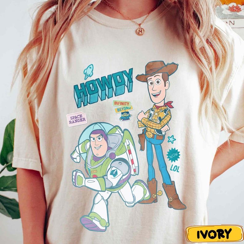 Peut inclure: T-shirt ivoire avec les personnages de dessins anim&eacute;s Buzz l'&Eacute;clair et Woody. Buzz est en position de course et Woody se tient les bras crois&eacute;s. Le t-shirt porte le mot "HOWDY" en turquoise et d'autres graphiques.
