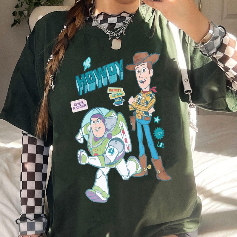 Peut inclure: T-shirt vert fonc&eacute; avec Buzz l'&Eacute;clair et Woody de Toy Story. Le t-shirt porte le mot "HOWDY" en bleu et l'expression "SPACE RANGER" dans un encadr&eacute; blanc. Buzz l'&Eacute;clair est en position de course et Woody est debout.