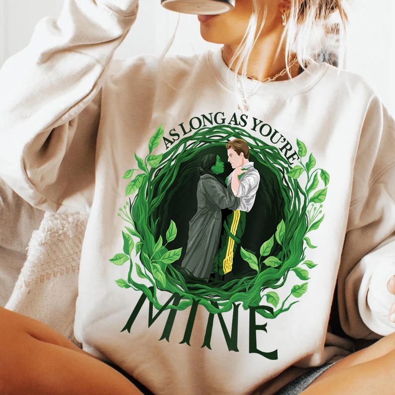 May include: A cream-coloured sweatshirt with a green and black illustration of two figures embracing within a leafy wreath. The text "AS LONG AS YOU'RE" arches above the image, with "MINE" below.
