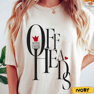 May include: Ivory-coloured t-shirt with the text "OFF WITH THEIR HEADS" in black, featuring a red crown and heart. The shirt has short sleeves and a crew neck.