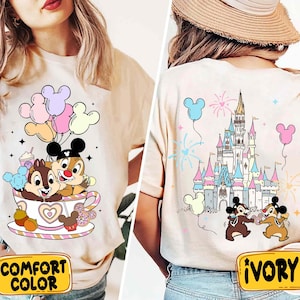 May include: A beige t-shirt with a cartoon image of Chip and Dale in a teacup with balloons. The back of the shirt has a cartoon image of Cinderella's castle with fireworks and Chip and Dale. The shirt has the words "Comfort Color" on the front and "Ivory" on the back.
