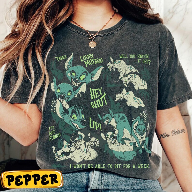 May include: Dark gray t-shirt featuring a graphic of cartoon hyenas in shades of green and white, with text that reads "That Lousy Mufasa!" and "Hey Shut Up!" Additional text includes "It's Not Funny!" and "I Won't Be Able to Sit for a Week."