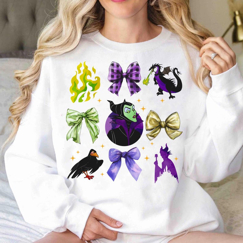 May include: White sweatshirt featuring colorful illustrations of bows, a dragon, a raven, and a silhouette of a castle. The design includes a green flame, a purple bow, a green bow, a gold bow, and a purple bow.