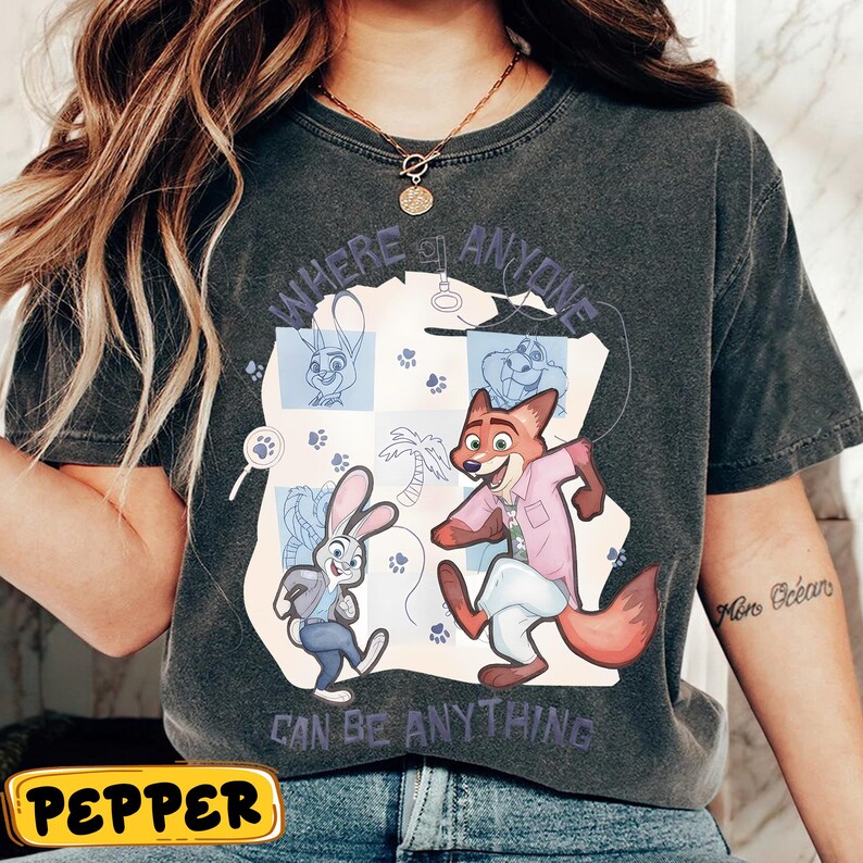 Pode incluir: T-shirt cinzento escuro com uma ilustra&ccedil;&atilde;o de desenho animado de personagens de Zootopia. O design inclui o texto "WHERE ANYONE CAN BE ANYTHING" e pegadas. A camisa tem um visual vintage e lavado.