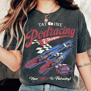 以下が含まれることがあります： スターウォーズのポッドレーサーのヴィンテージスタイルのグラフィックがプリントされた黒いTシャツ。グラフィックには、「タトゥイーン・ポッドレーシング・チャンピオン」と「Now This Is Podracing!」のテキストと、アナキン・スカイウォーカーのポッドレーサーの画像が描かれています。