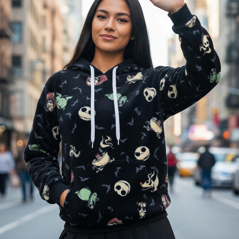 May include: Black hooded sweatshirt featuring a pattern of characters and bats from The Nightmare Before Christmas. The sweatshirt has a white drawstring and a front pocket. The sleeves and bottom hem are black.