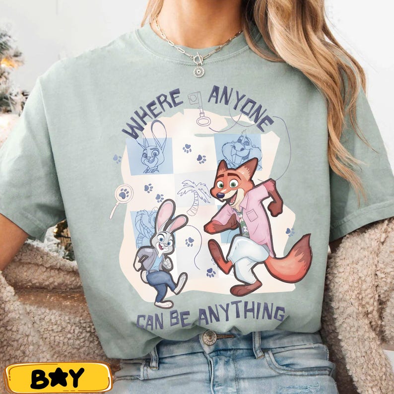 Pode incluir: Camiseta verde claro com personagens de desenho animado de Zootopia. O design inclui Judy Hopps e Nick Wilde, junto com o texto "WHERE ANYONE CAN BE ANYTHING". A camiseta tem gola redonda e mangas curtas.